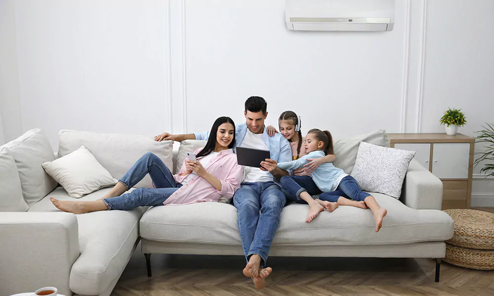 A family relaxing on a sofa in a cool, comfortable living room with a wall-mounted air conditioner